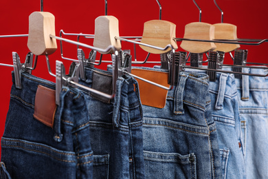 Rack with different jeans on red background, closeup