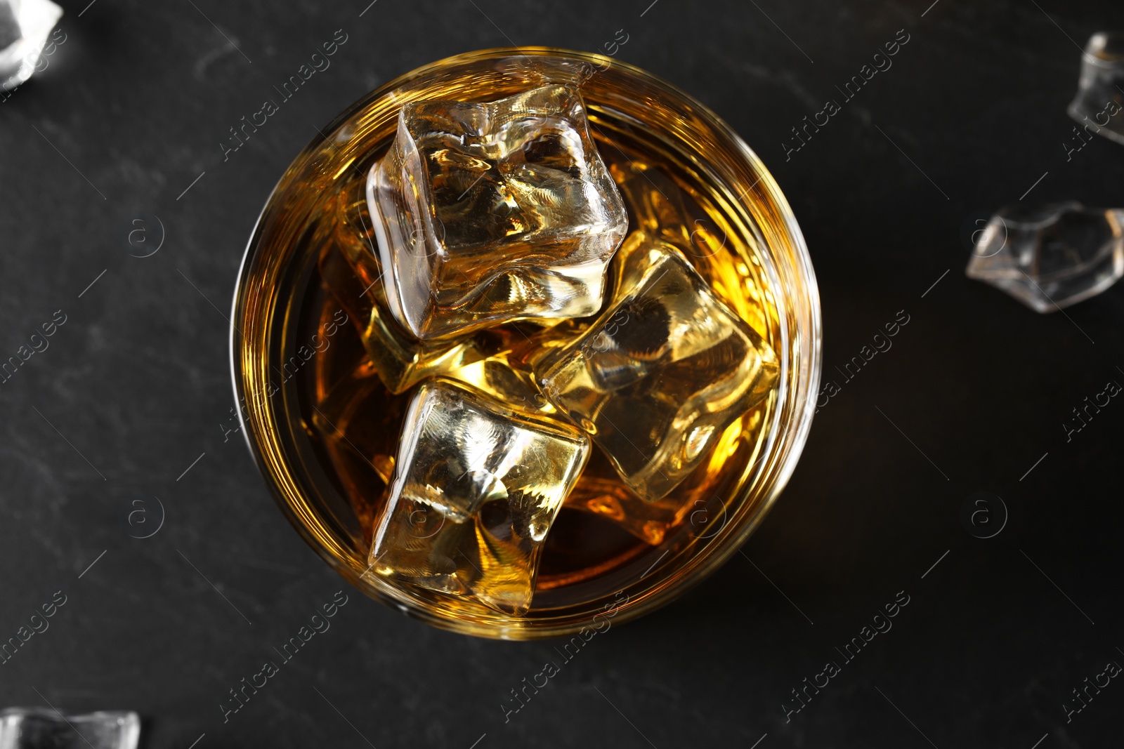 Photo of Whiskey and ice cubes in glass on black table, top view