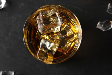 Photo of Whiskey and ice cubes in glass on black table, top view