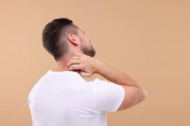 Allergy symptom. Man scratching his neck on light brown background. Space for text