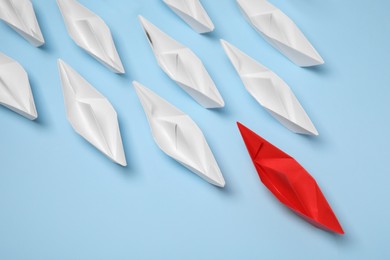 Photo of Paper boats following red one on light blue background. Leadership concept
