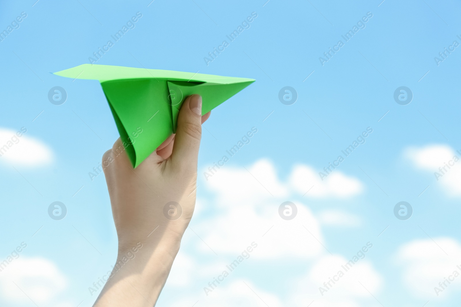 Photo of Woman holding paper plane against blue sky, closeup. Space for text