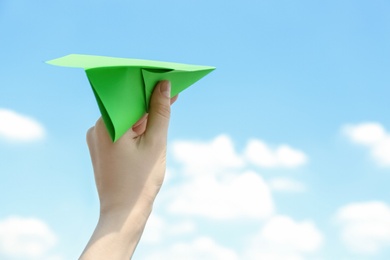 Photo of Woman holding paper plane against blue sky, closeup. Space for text