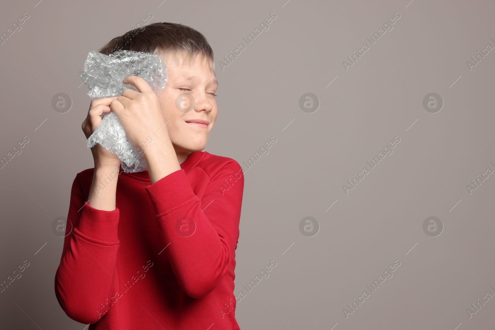 Photo of Boy popping bubble wrap on beige background, space for text. Stress relief