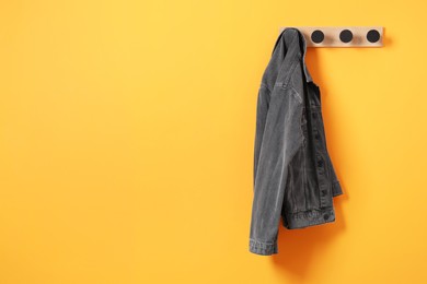 Photo of Rack with dark gray denim jacket on orange wall, space for text