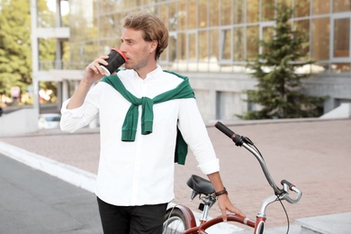 Photo of Attractive man with bike and cup of coffee on city street