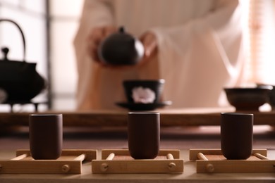 Photo of Master conducting traditional tea ceremony at table indoors, focus on cups