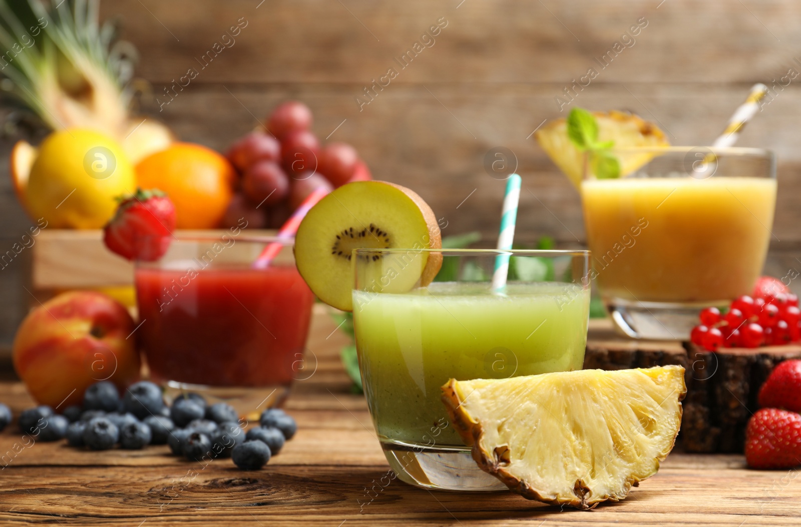 Photo of Delicious colorful juices in glasses and fresh ingredients on wooden table