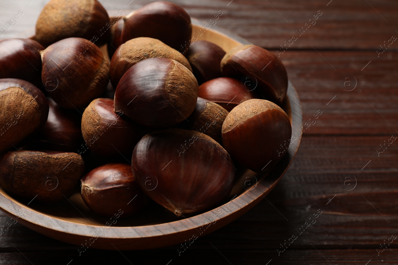 Photo of Sweet fresh edible chestnuts in bowl on wooden table, closeup