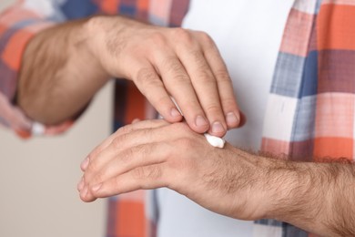 Man applying cream onto hand on beige background, closeup