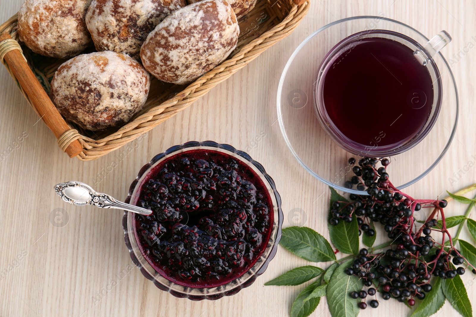 Photo of Elderberry jam, glass cup of tea, tasty cookies and Sambucus berries on wooden table, flat lay