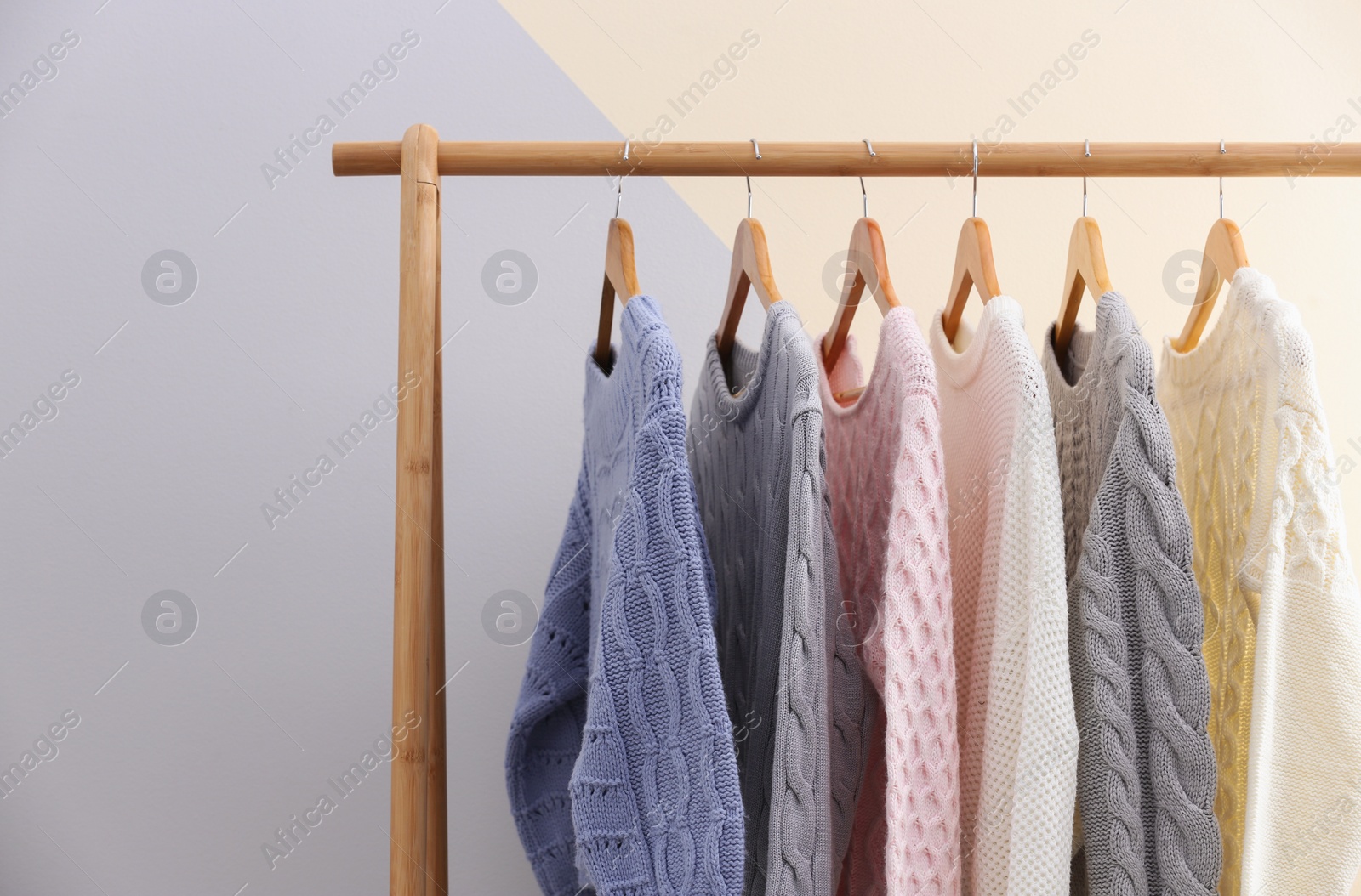 Photo of Collection of warm sweaters hanging on rack near color wall