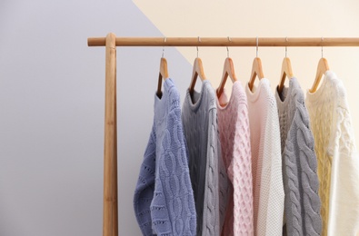 Photo of Collection of warm sweaters hanging on rack near color wall