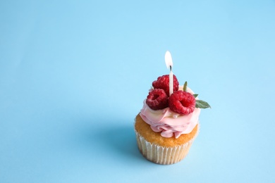 Delicious birthday cupcake with raspberries and burning candle on light blue background. Space for text