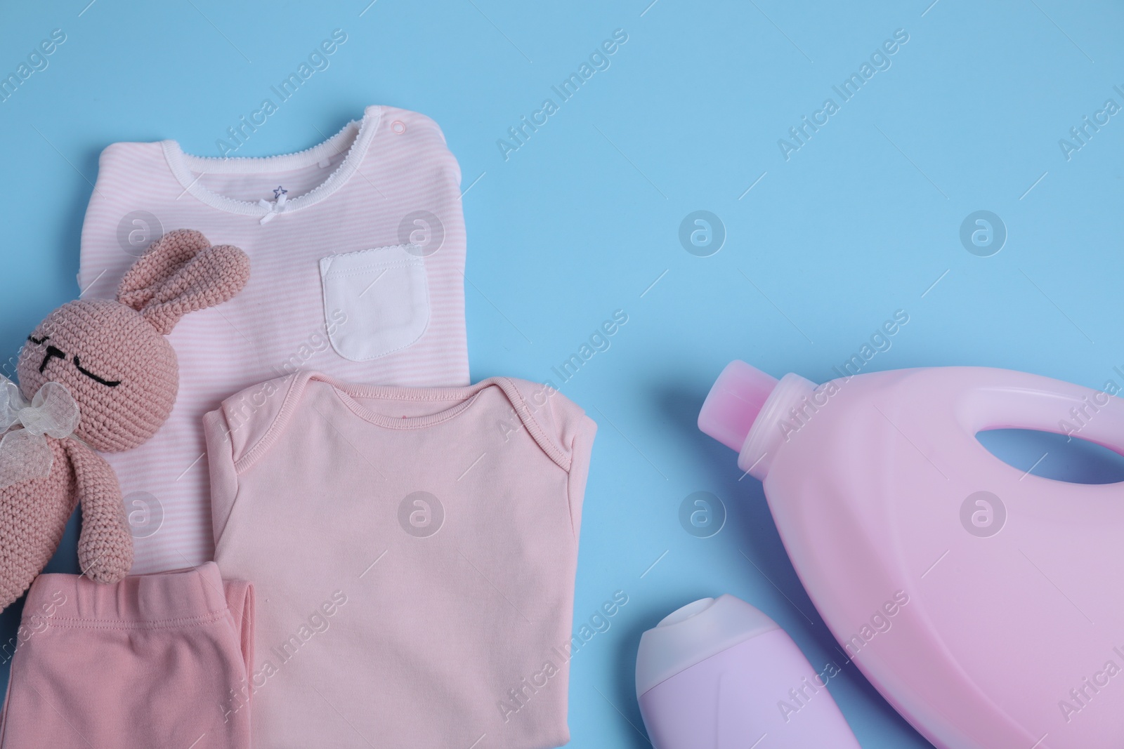 Photo of Bottles of laundry detergents, baby clothes and toy bear on light blue background, flat lay. Space for text