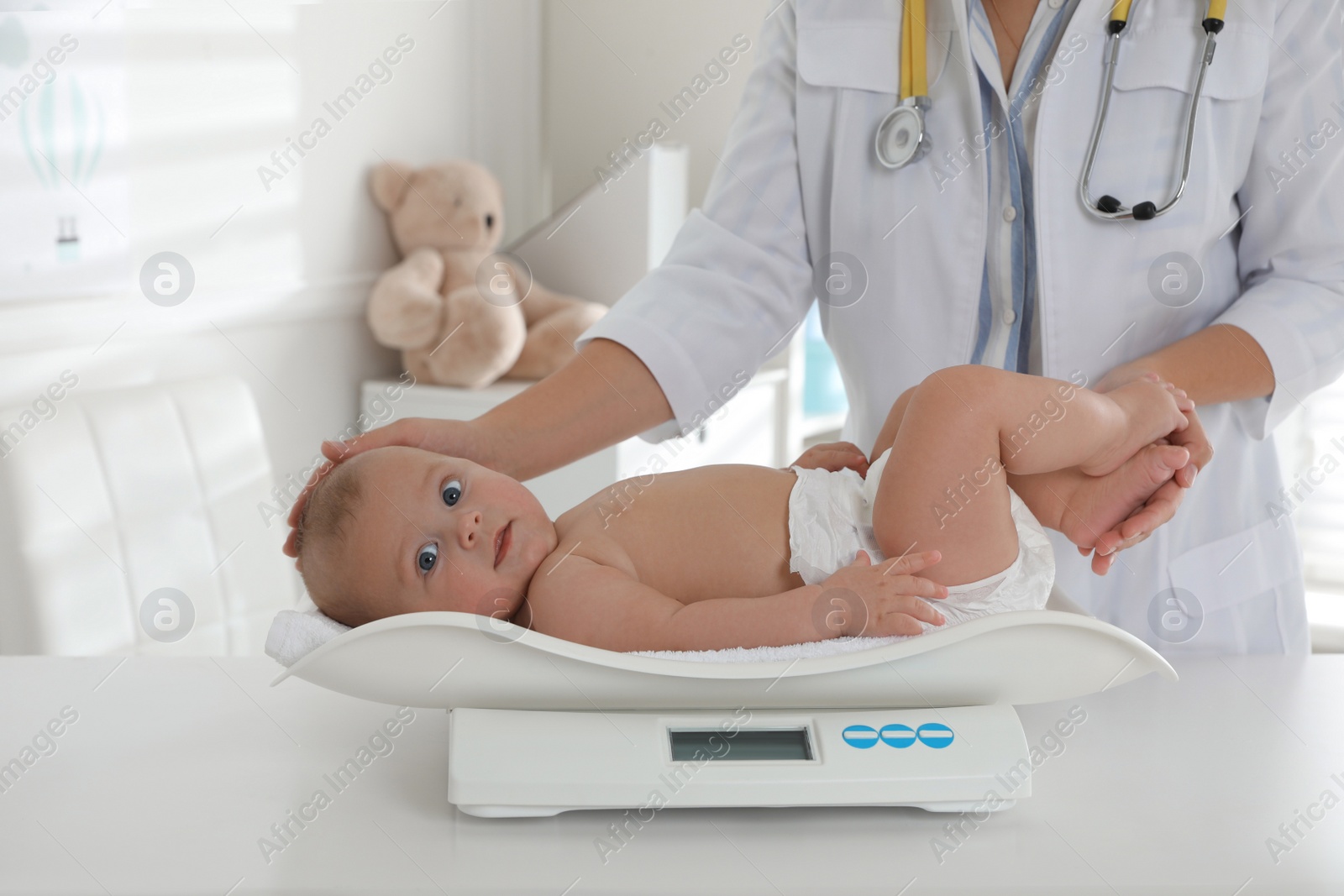 Photo of Pediatrician weighting cute baby in clinic, closeup. Health care