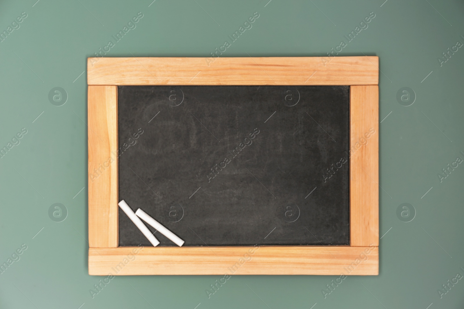 Photo of Small clean blackboard with chalk hanging on color wall