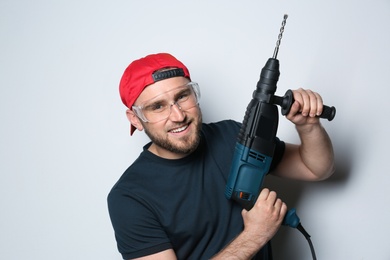 Photo of Young working man with rotary hammer on light background