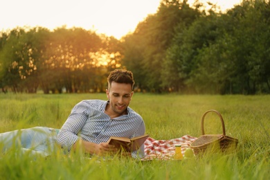 Photo of Young man reading book on picnic blanket in park