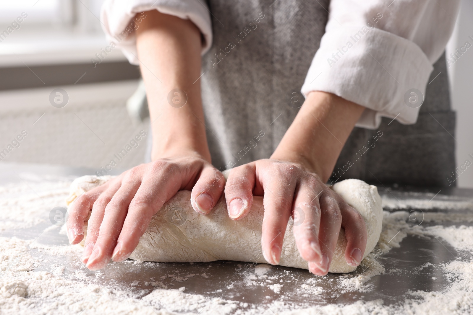 Photo of Woman kneading dough at table in kitchen, closeup