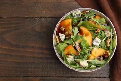 Photo of Tasty salad with persimmon, blue cheese and walnuts served on wooden table, top view. Space for text