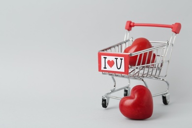 Small shopping cart with phrase I Love You and decorative hearts on light grey background, space for text