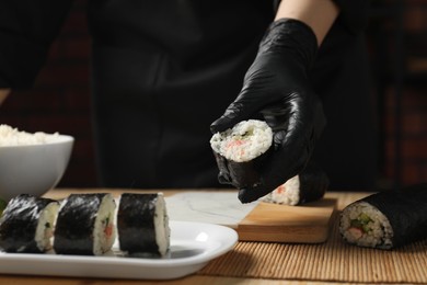 Chef in gloves putting sushi roll onto dish at table, closeup