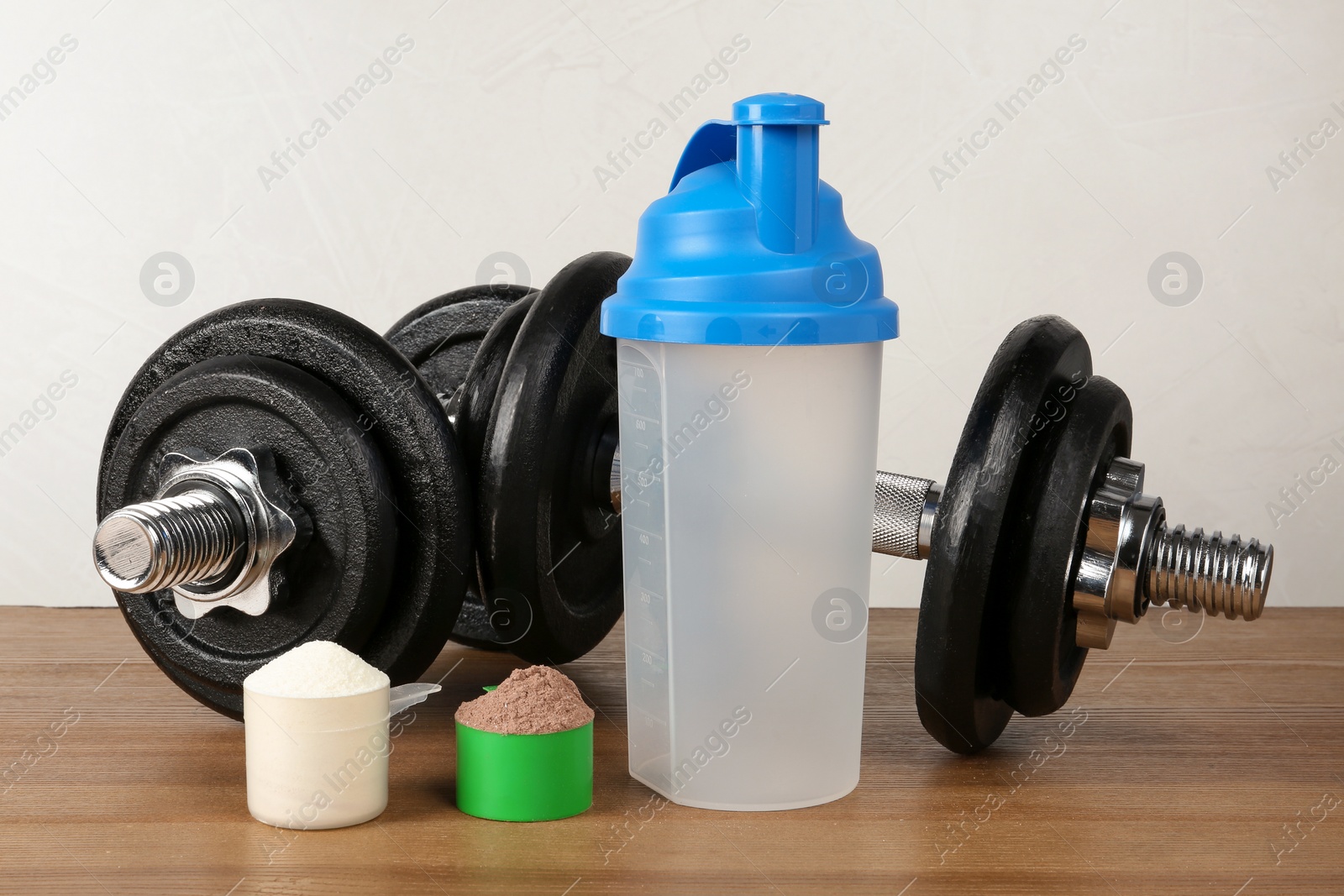 Photo of Empty protein shake sport bottle, scoops with powders and dumbbells on table