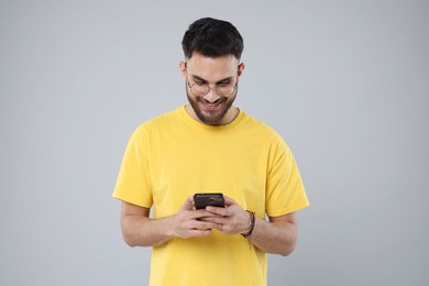 Happy young man using smartphone on grey background
