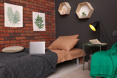 Stylish teenager's room with laptop on bed near brick wall