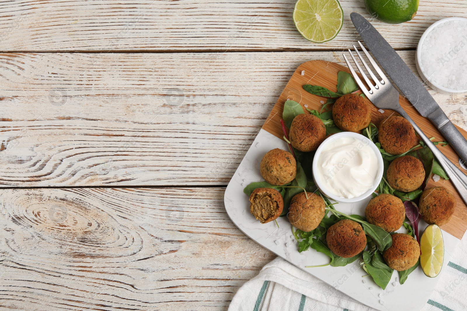 Photo of Delicious falafel balls with herbs, lime and sauce on wooden table, flat lay. Space for text