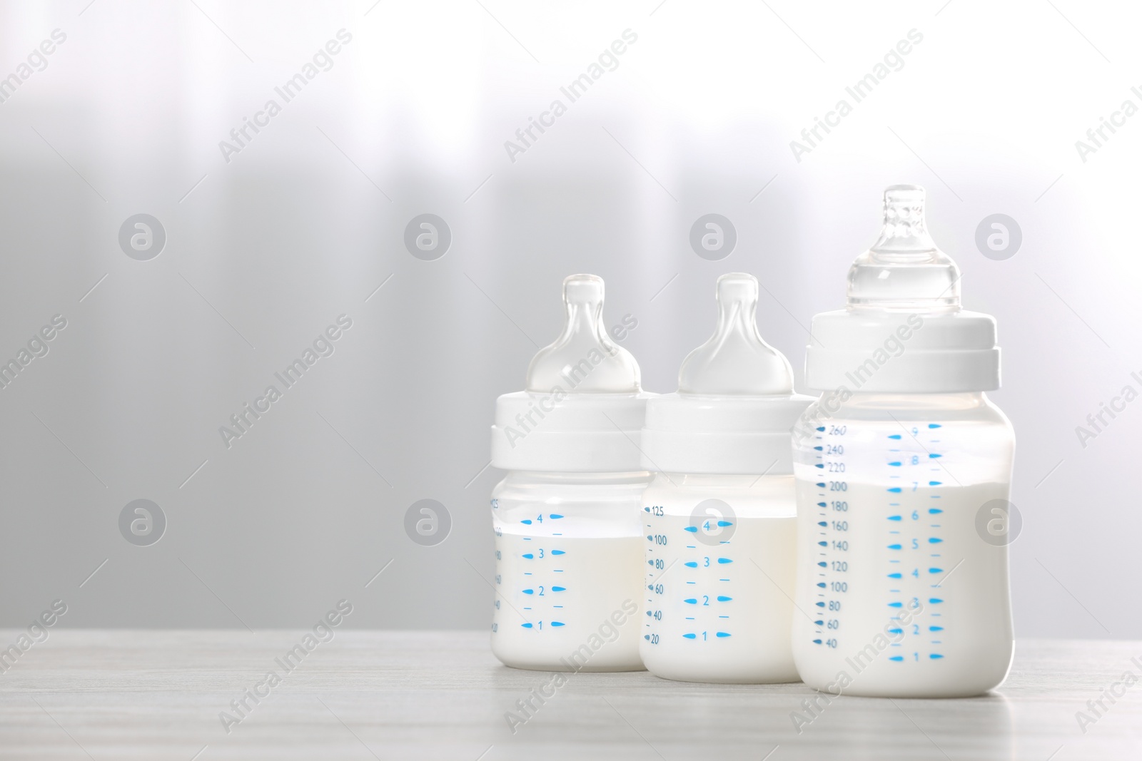 Photo of Feeding bottles with infant formula on white wooden table indoors. Space for text