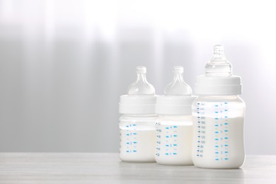 Feeding bottles with infant formula on white wooden table indoors. Space for text