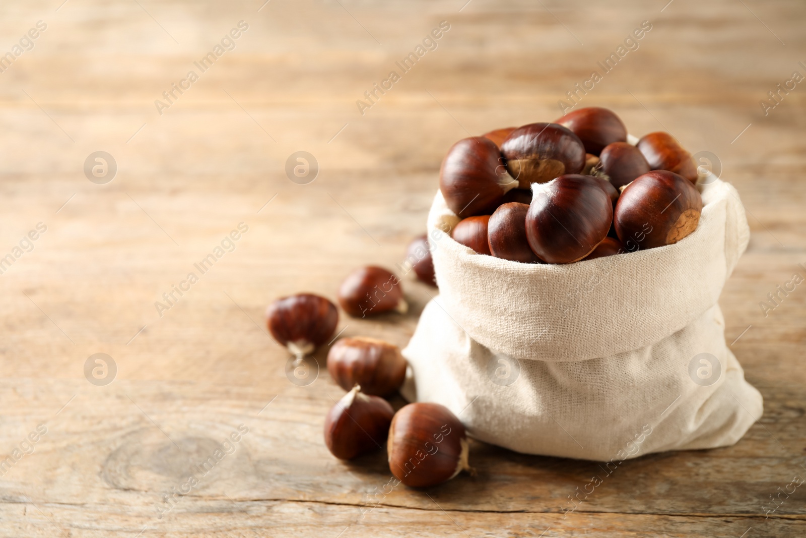 Photo of Fresh sweet edible chestnuts in sack on wooden table. Space for text