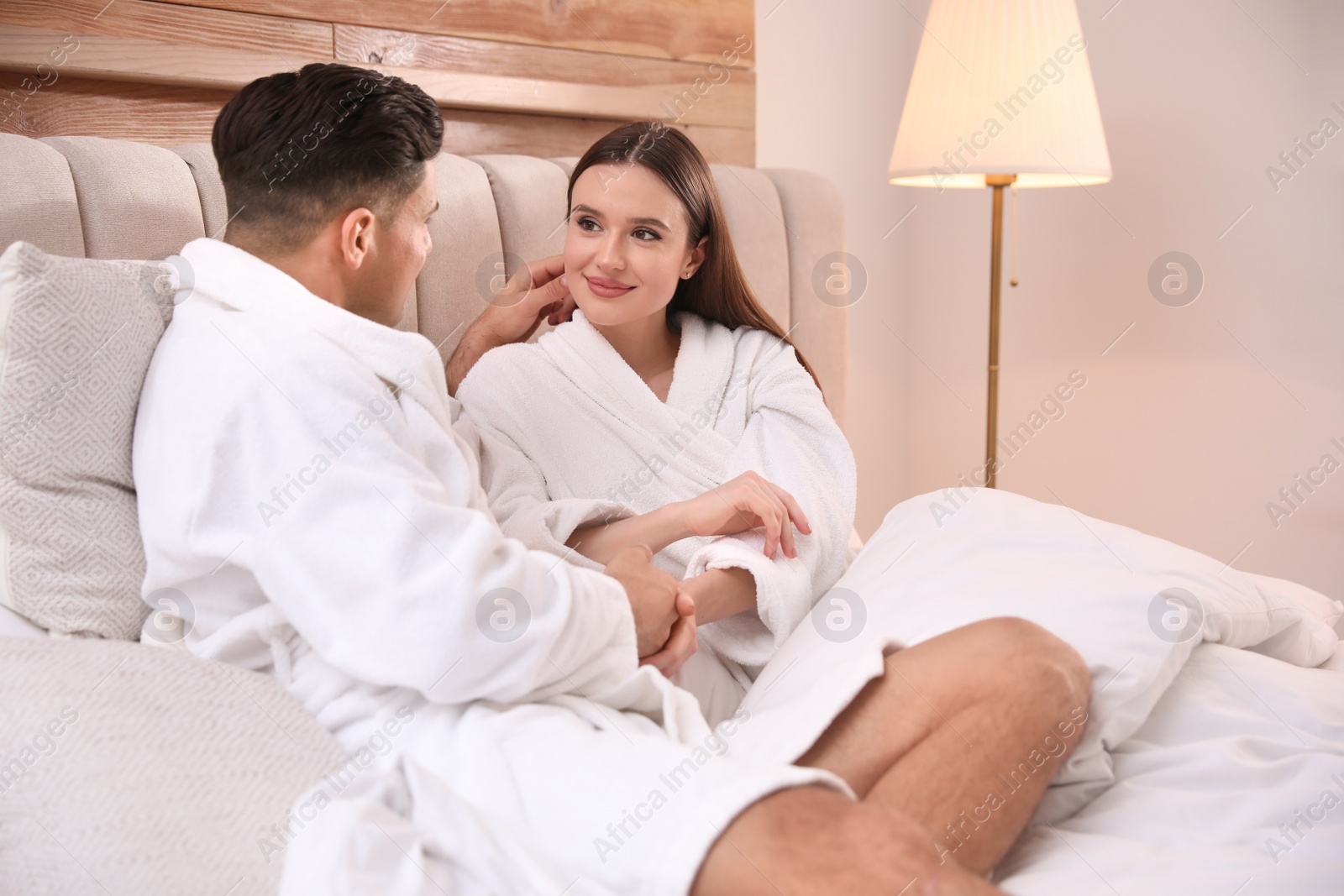 Photo of Happy couple in bathrobes resting on bed at home