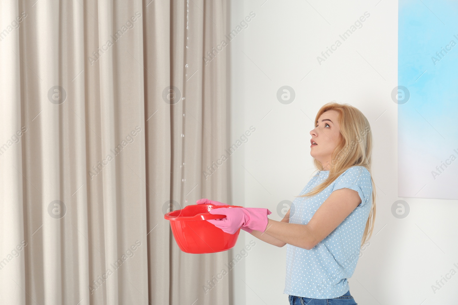 Photo of Woman holding plastic basin under water leakage from ceiling at home