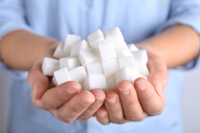 Photo of Woman holding heap of refined sugar cubes, closeup