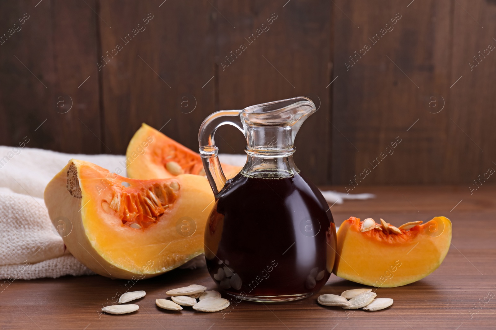 Photo of Fresh pumpkin seed oil in glass jug on wooden table