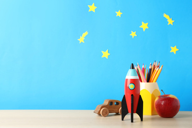 Photo of Rocket, pencils, toy car and apple on wooden table, space for text. Back to school