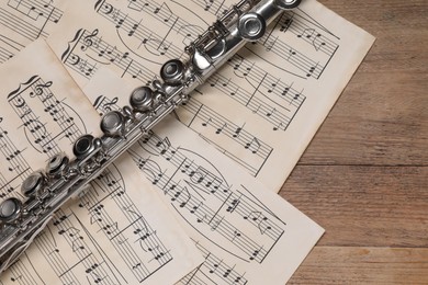 Photo of Sheets with musical notes and flute on wooden table, flat lay