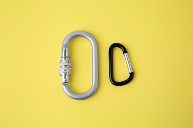 Photo of Two metal carabiners on yellow background, flat lay