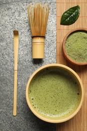 Photo of Cup of fresh matcha tea, bamboo whisk, spoon and green powder on grey table, flat lay