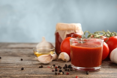 Photo of Composition with glass of tasty tomato sauce on wooden table against color background. Space for text