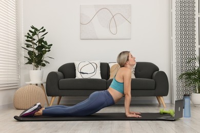 Online fitness trainer. Woman doing exercise near laptop at home