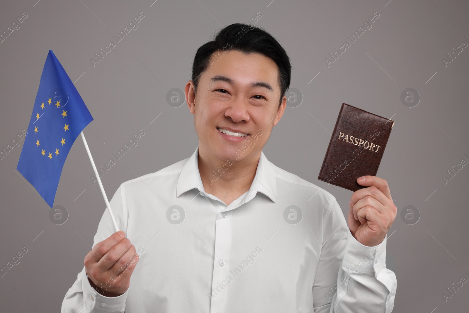 Photo of Immigration. Happy man with passport and flag of European Union on grey background