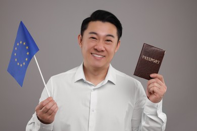 Immigration. Happy man with passport and flag of European Union on grey background