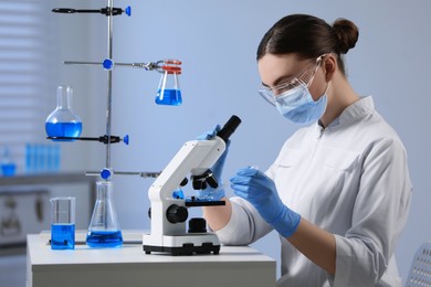 Scientist dripping sample onto Petri dish while working with microscope in laboratory