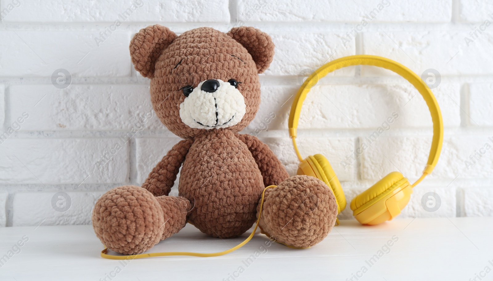 Photo of Baby songs. Toy bear and yellow headphones on white wooden table