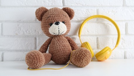 Baby songs. Toy bear and yellow headphones on white wooden table