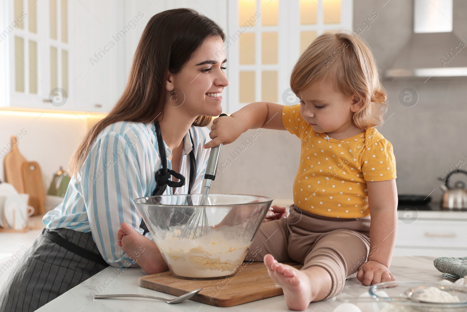 Photo of Mother and her little daughter cooking dough together in kitchen